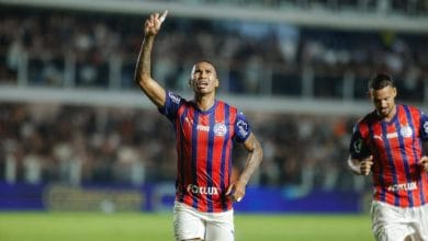Jogador do Bahia no campo com o uniforme do clube apontando para cima