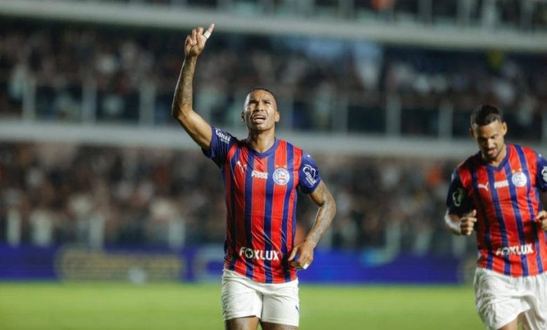 Jogador do Bahia no campo com o uniforme do clube apontando para cima